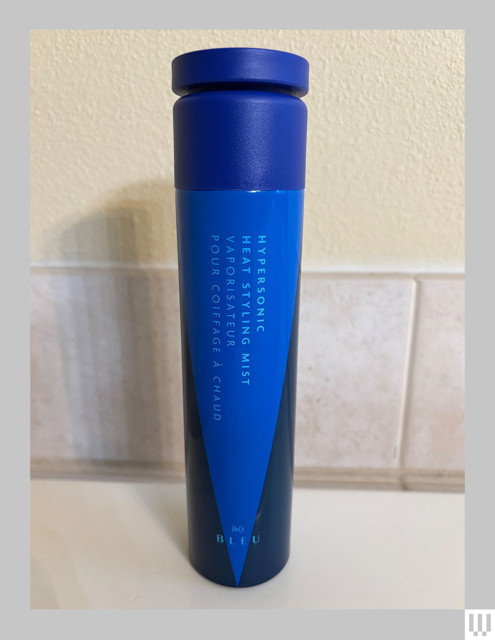 R and Co Bleu Hypersonic Heat Styling Mist a narrow cylindrical blue bottle on a beige countertop